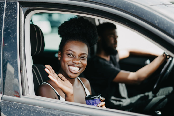 A driver welcoming a rider beside a car